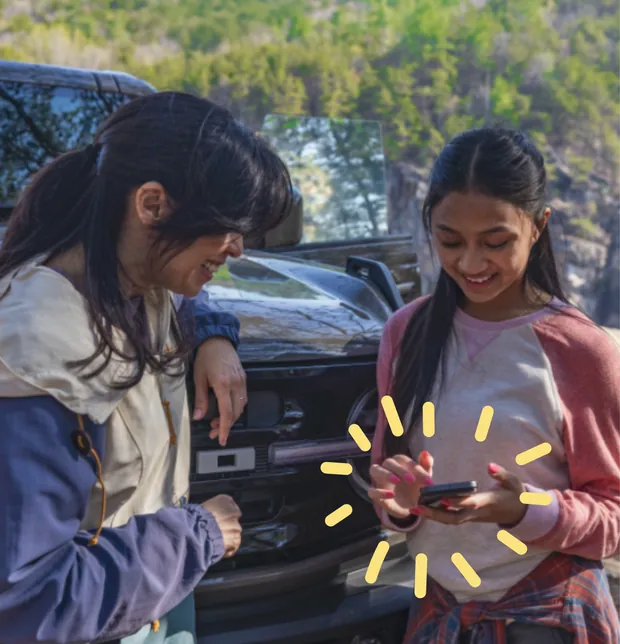 Two people reading a guidebook on a phone at the tailgate of a truck